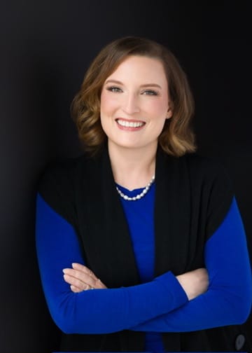 Nicole Eisdorfer smiling with arms crossed, wearing a blue sweater and black vest